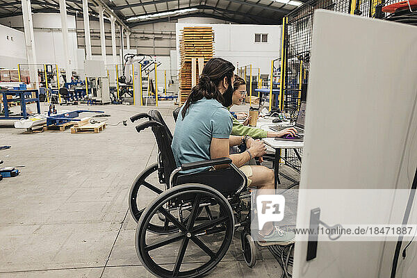 Engineer sitting in wheelchair working with colleague in factory