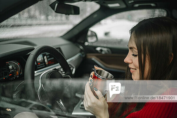 Smiling woman having coffee sitting in car