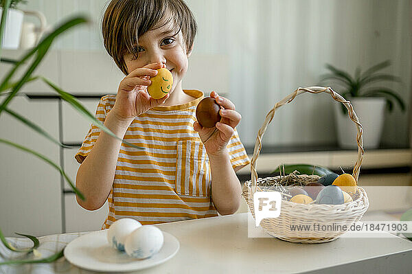 Smiling boy holding decorated Easter eggs at home