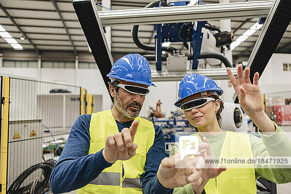 Mature engineer with colleague wearing smart glasses in robotics factory