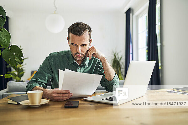 Worried businessman doing paperwork sitting at table working from home