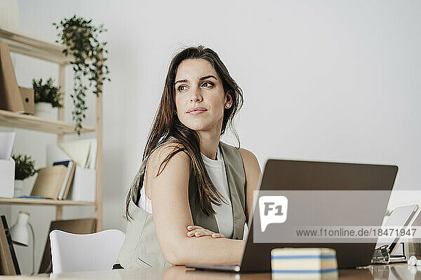 Thoughtful businesswoman sitting with laptop in office
