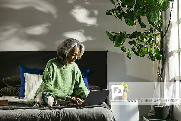 Frau benutzt Laptop auf dem Bett im Schlafzimmer zu Hause