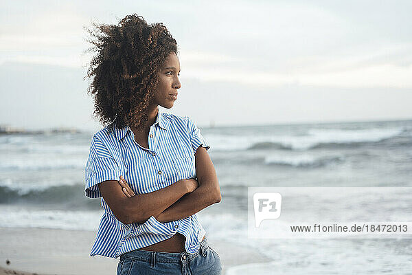 Contemplative woman standing with arms crossed at beach