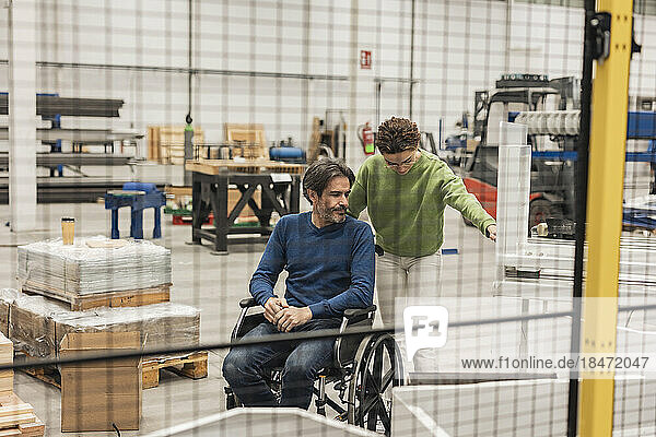 Mature engineer sitting in wheelchair discussing with colleague in factory