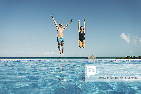 Sorgloses Paar springt mit erhobenen Armen im Schwimmbad