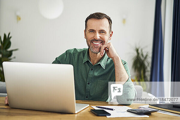 Mann sitzt am Schreibtisch mit Laptop und arbeitet von zu Hause aus