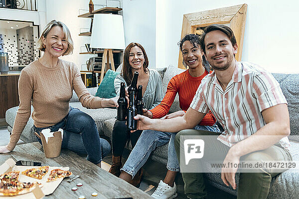 Happy businesswomen and businessman toasting beer bottles on sofa at office