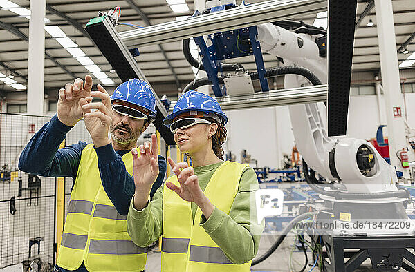 Mature engineers wearing smart glasses in robotics factory