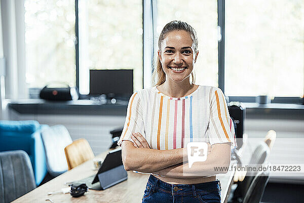 Happy businesswoman with arms crossed standing at office