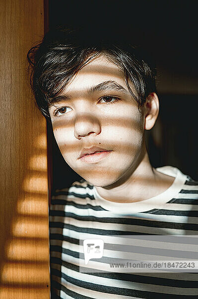 Thoughtful teenage boy with sunlight on face standing by door