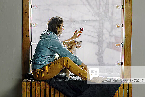 Woman with dog sticking heart sticker on glass window at home