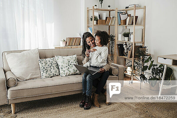 Lächelndes Mädchen und Mutter sitzen mit Laptop auf dem Sofa zu Hause