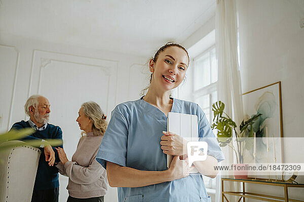 Smiling nurse holding tablet PC with senior man and woman at home