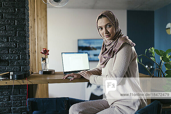 Freelancer wearing hijab sitting at table in home office
