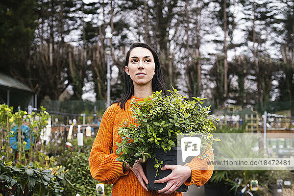 Young woman with potted plant standing in garden center