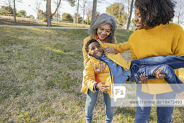 Verspielte Frauen tragen einen Jungen und genießen ihn im Park