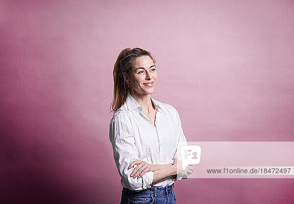 Contemplative businesswoman standing with arms crossed against colored background