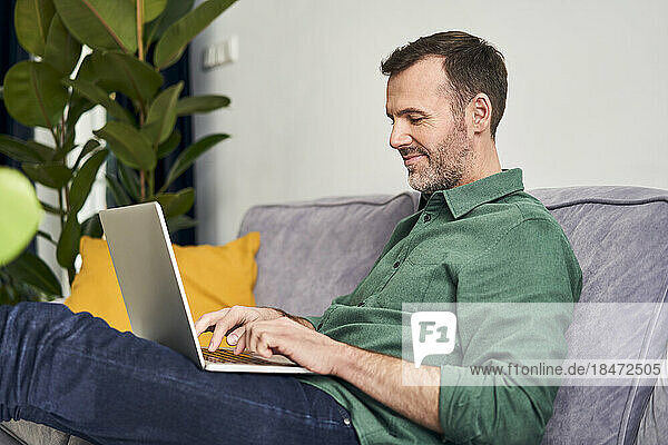 Relaxed man working from home using laptop sitting on the sofa
