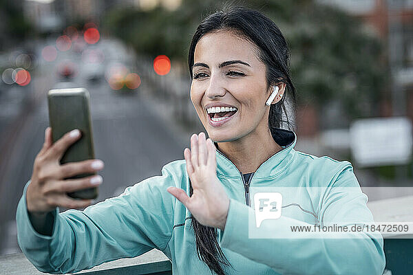 Happy young woman waving on video call through mobile phone