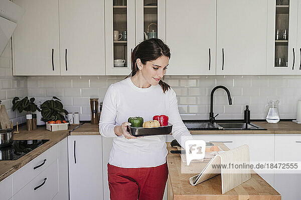 Woman with vegetable using tablet PC in kitchen at home