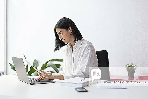 Businesswoman with document typing on laptop at desk