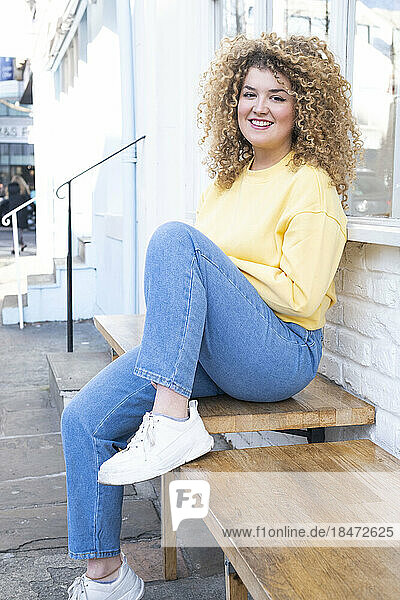 Smiling woman with curly hair sitting on bench