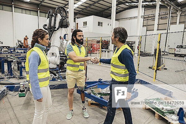Engineer with colleagues shaking hand in factory