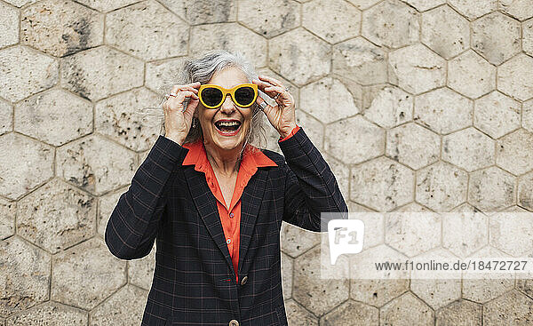 Happy mature businesswoman wearing sunglasses enjoying in front of wall