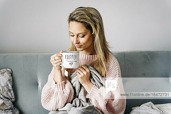 Smiling young woman drinking coffee sitting on sofa at home