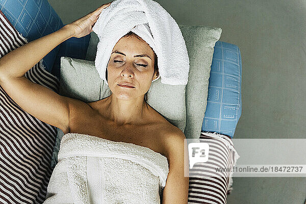 Woman wearing towel relaxing on sofa at home