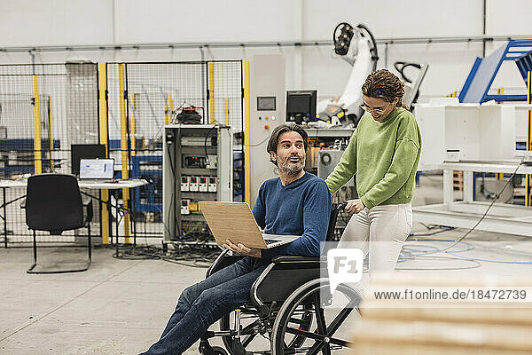 Engineer pushing colleague sitting in wheelchair with laptop