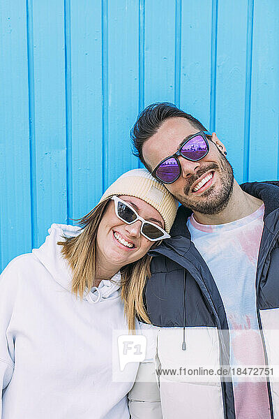 Lächelnder Freund und Freundin mit Sonnenbrille vor der Wand