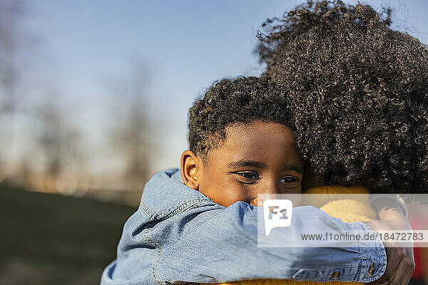 Boy embracing mother in park on sunny day