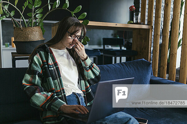 Tired young student sitting with laptop on sofa at home