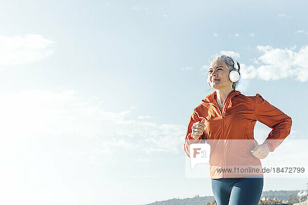 Mature woman listening to music through headphones and jogging on sunny day