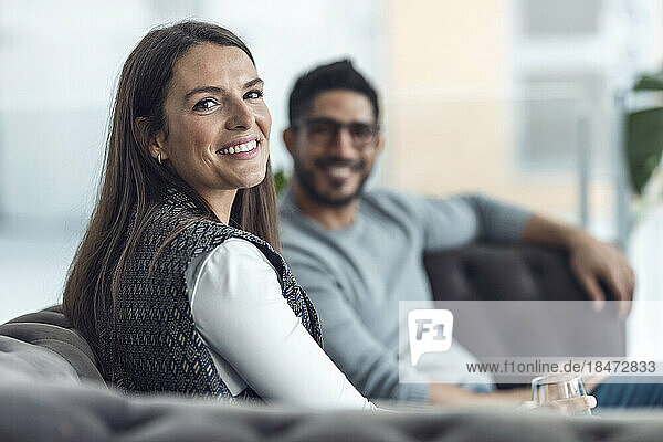 Happy businesswoman with colleague sitting on sofa at office