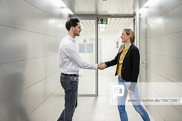 Smiling businesswoman shaking hand with colleague in corridor at factory