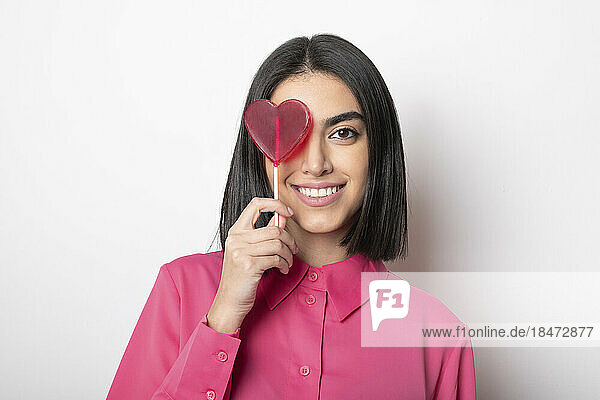 Happy woman with heart shaped lollipop against white background