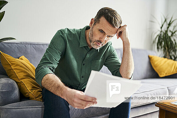 Worried man looking at documents sitting on sofa