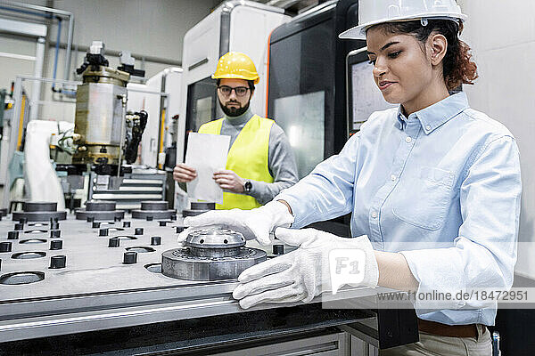 Lächelnde Geschäftsfrau  die in der Fabrik mit Maschinenteilen arbeitet