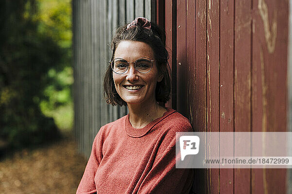 Glückliche Frau mit Brille lehnt an Holzwand