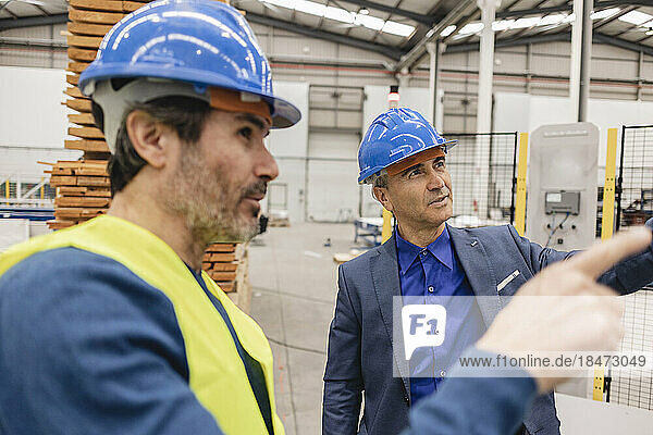 Mature engineers wearing hardhat having discussions in robotics factory