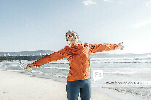 Smiling mature woman standing with arms outstretched on beach