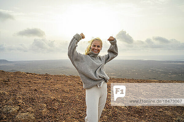 Happy young woman flexing muscles standing on mountain