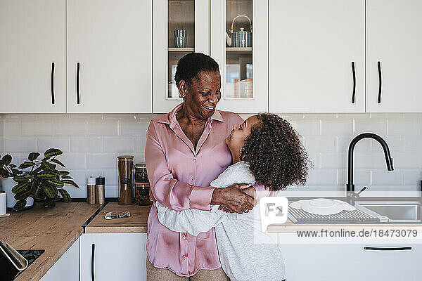 Grandmother embracing granddaughter in kitchen at home