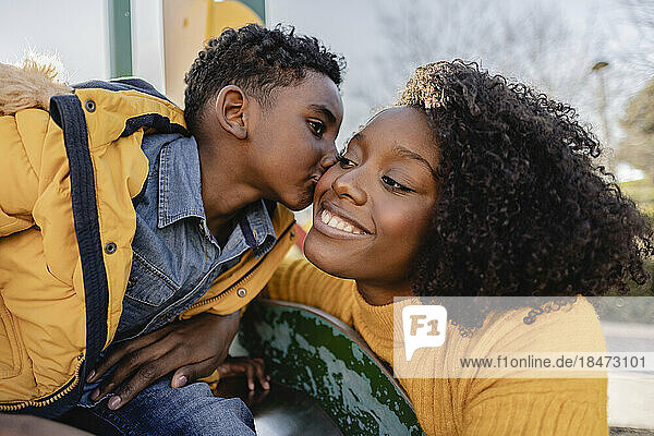 Boy kissing cheek of smiling mother in park