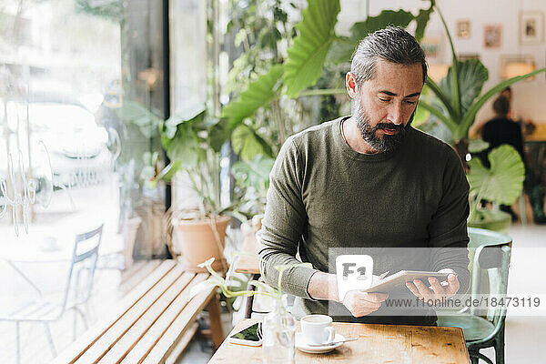 Mature man using tablet PC sitting at table in cafe