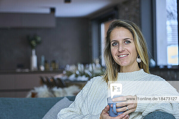 Happy woman with blond hair holding coffee cup at home