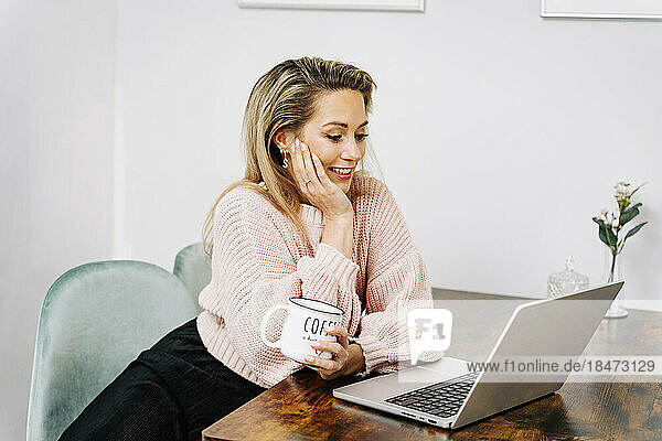Happy woman with coffee cup using laptop at home